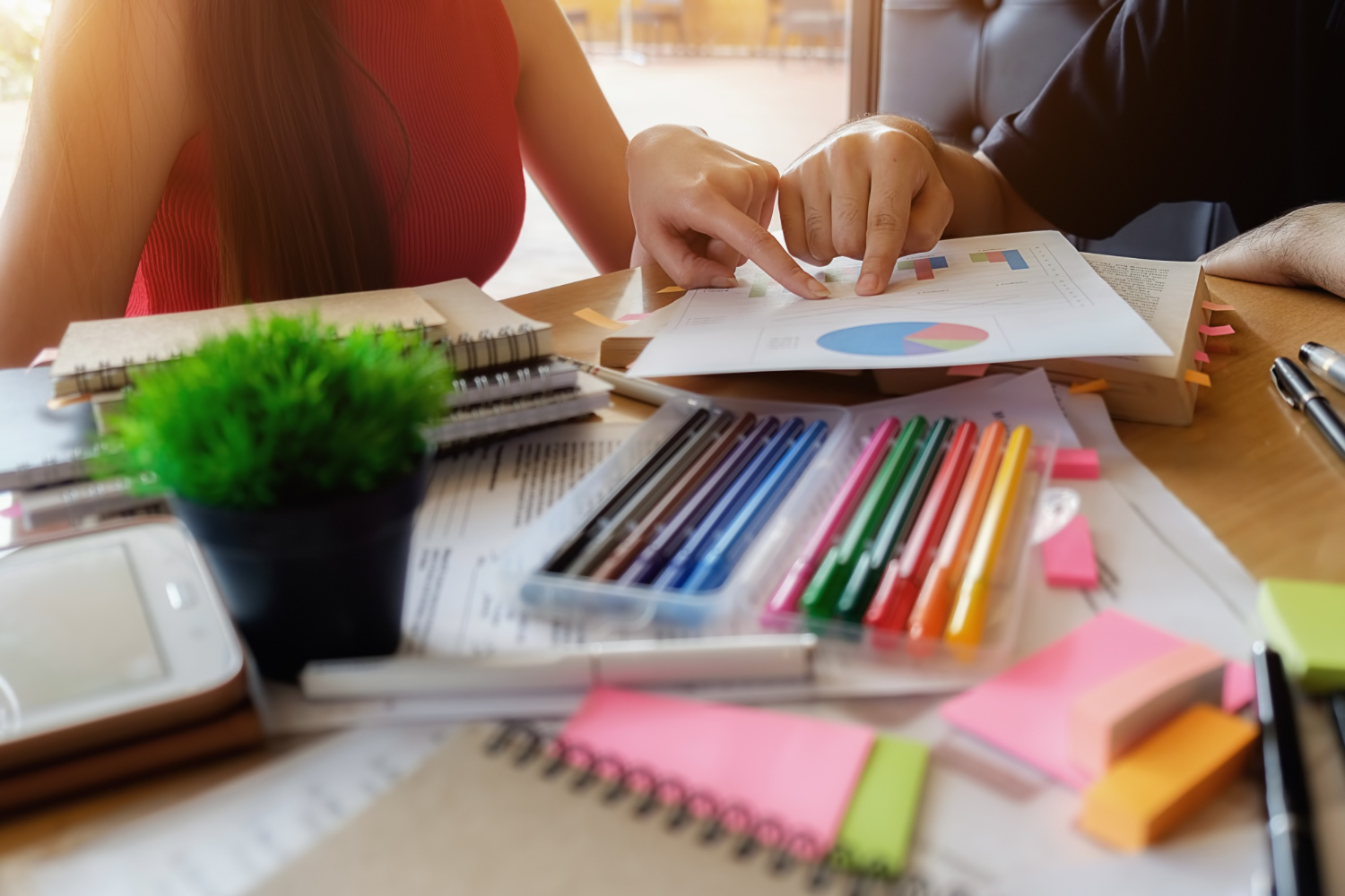 Persone alla scrivania, tra fogli con dati e grafici, e pennarelli