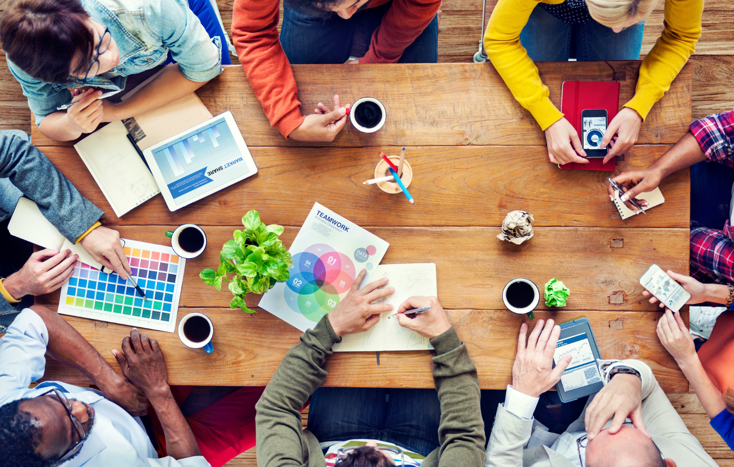 Tavolo di lavoro con più persone tra tazze di caffè, tablet e grafici