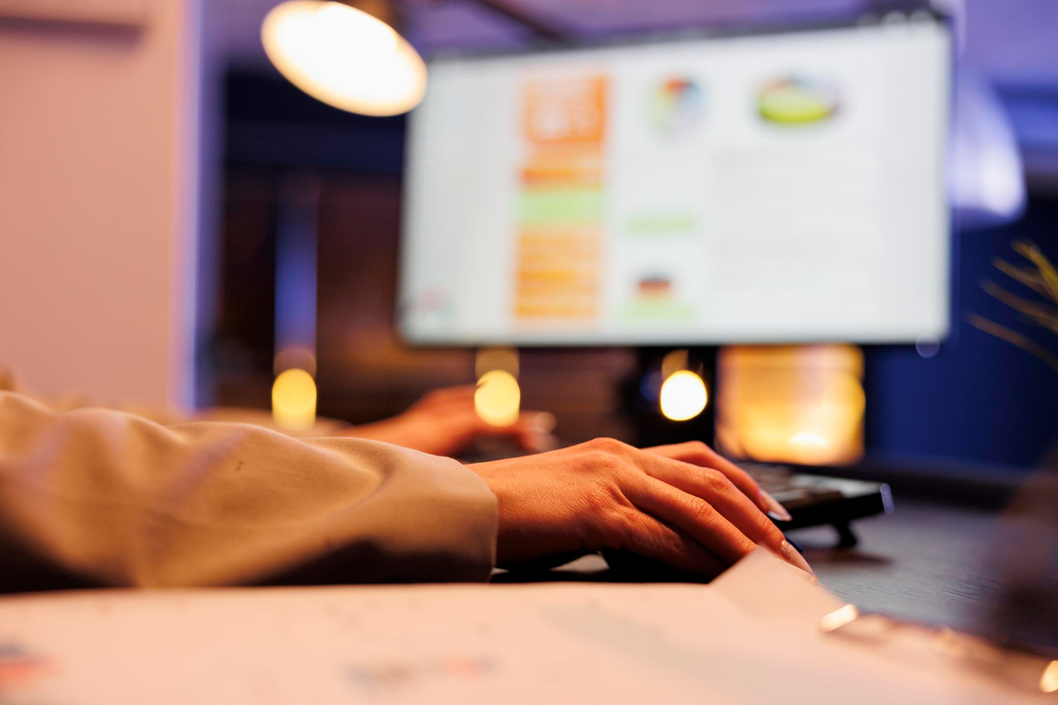 Mano maschile su un mouse, con sullo sfondo il monitor di un pc