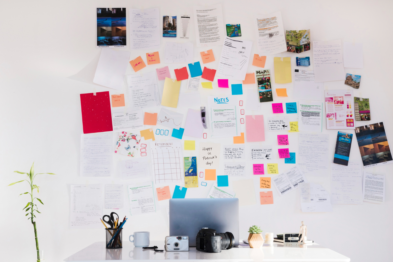 Parete ricca di post-it e fogli vari a fare da sfondo a una scrivania con laptop