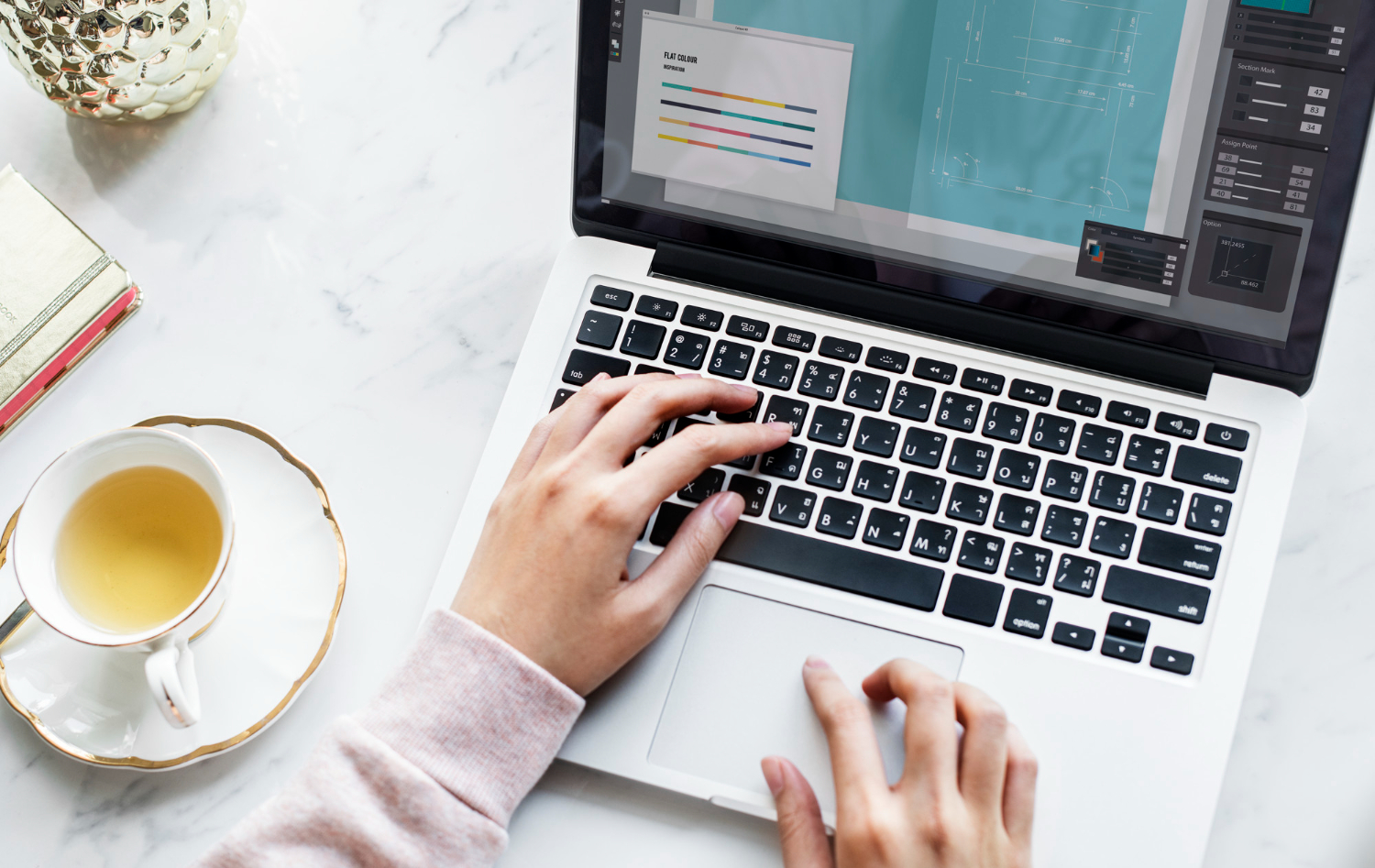 Mani di donna che digitano su un laptop con a fianco una tazza di tè